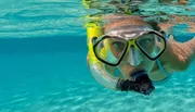 A person is half-submerged in clear blue water, wearing snorkeling gear.