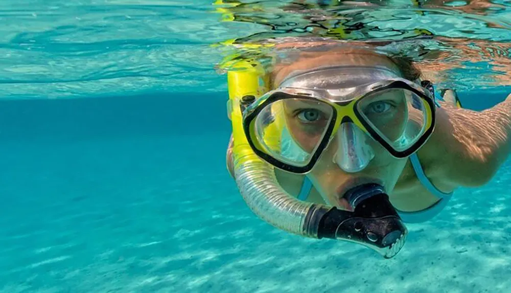 A person is half-submerged in clear blue water wearing snorkeling gear