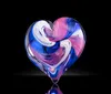 The image shows a beautifully crafted glass sculpture with vibrant blue and red colors resembling a sea creature or flower reflected on a dark surface