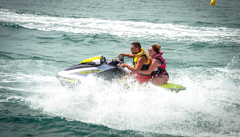 Two people are riding a jet ski across choppy water creating a spray behind them