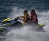 Two people are riding a jet ski across choppy water creating a spray behind them