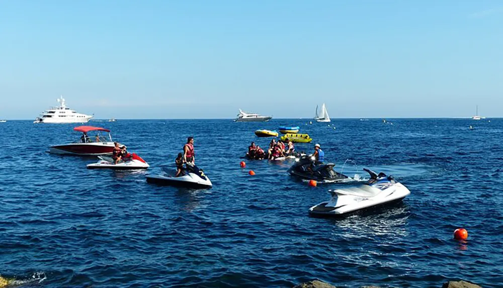 The image captures a bustling water scene with people engaged in various recreational activities on jet skis and boats against a backdrop of larger vessels and a clear blue sky