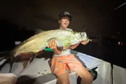 A person is proudly displaying a large fish they caught at night on a boat.