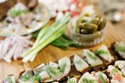 This image features an appetizing arrangement of open sandwiches with various toppings, surrounded by fresh ingredients and pickles, on a wooden surface.