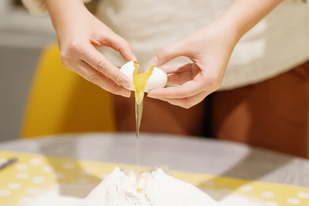 A person is cracking an egg open over a pile of flour likely preparing to mix ingredients for baking or cooking