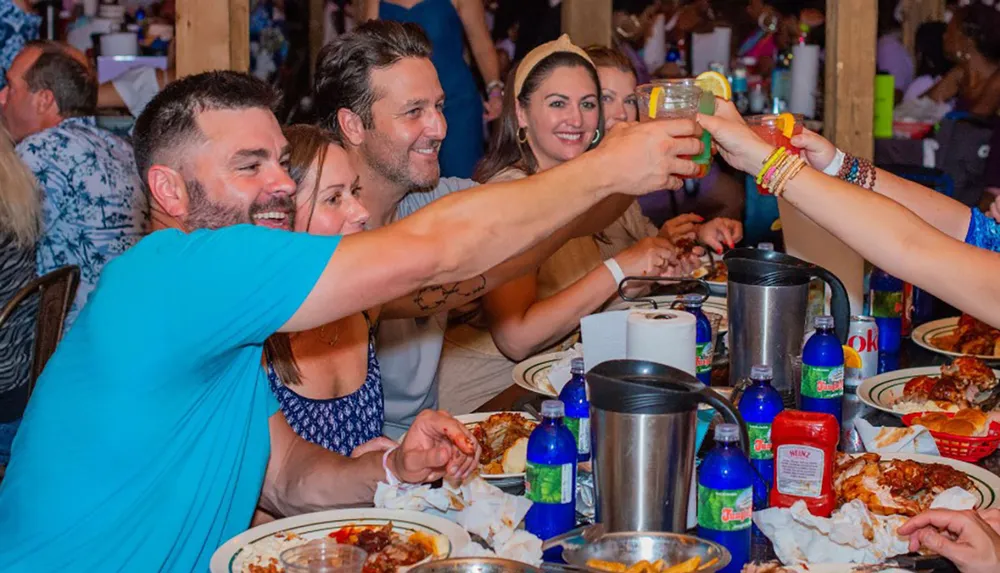 A group of people are toasting with drinks at a casual dining table littered with food remnants and condiments