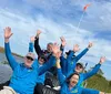 A group of people in matching blue shirts are joyfully raising their hands while on a boat ride under a clear blue sky