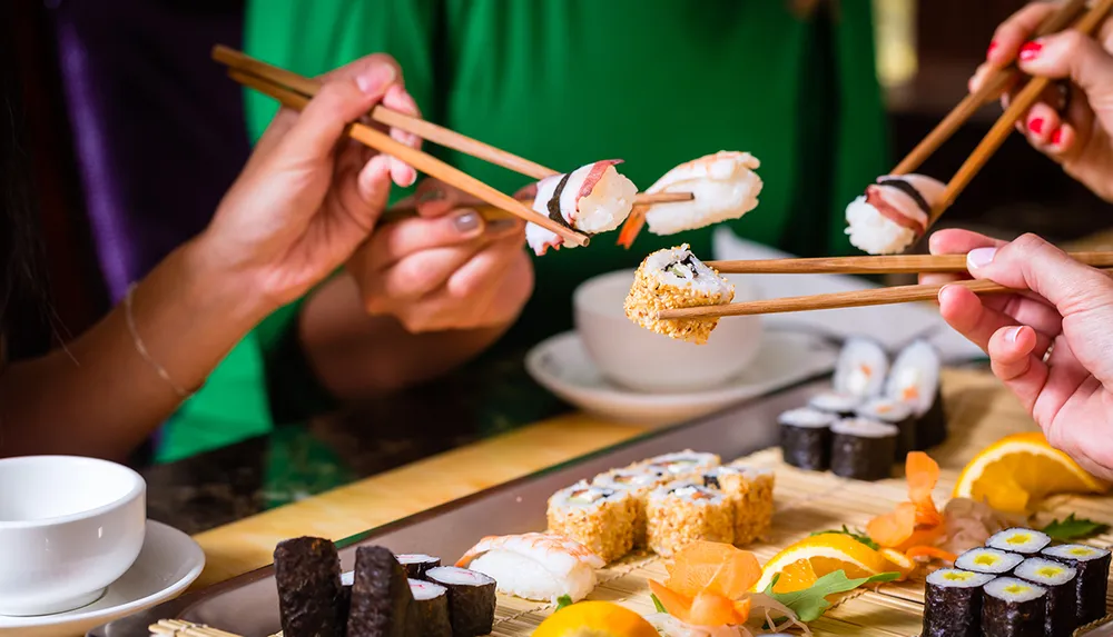 Two individuals are enjoying an assortment of sushi using chopsticks