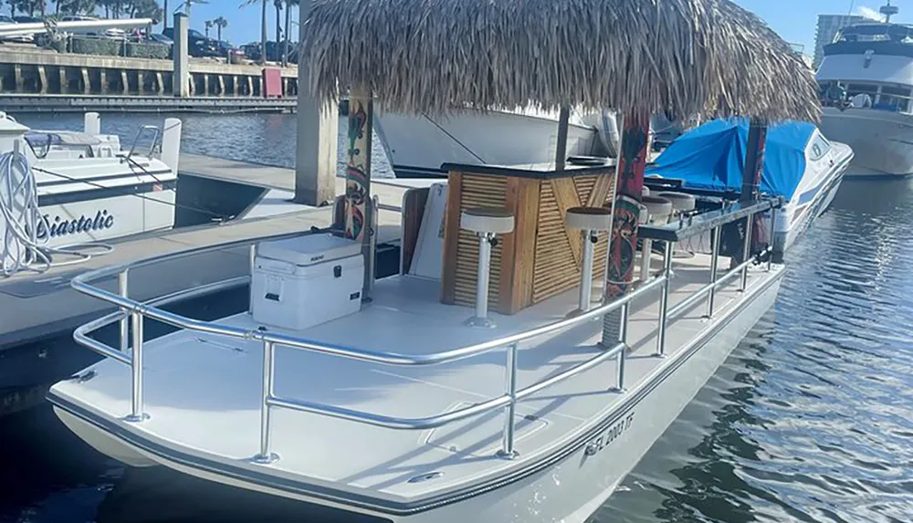 A pontoon boat equipped with a bar and stools is docked in a marina on a sunny day