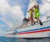 Two people wearing snorkeling gear are jumping off a sailboat into the sea while others watch