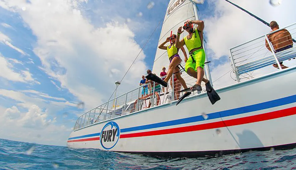 Two people wearing snorkeling gear are jumping off a sailboat into the sea while others watch