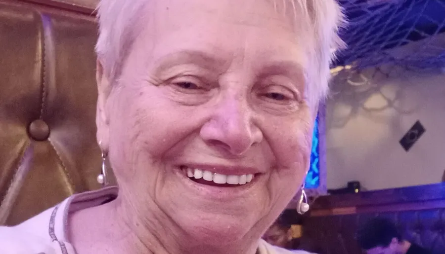 A smiling person with short hair and earrings is posing for a close-up photo in a room with a warm ambiance.