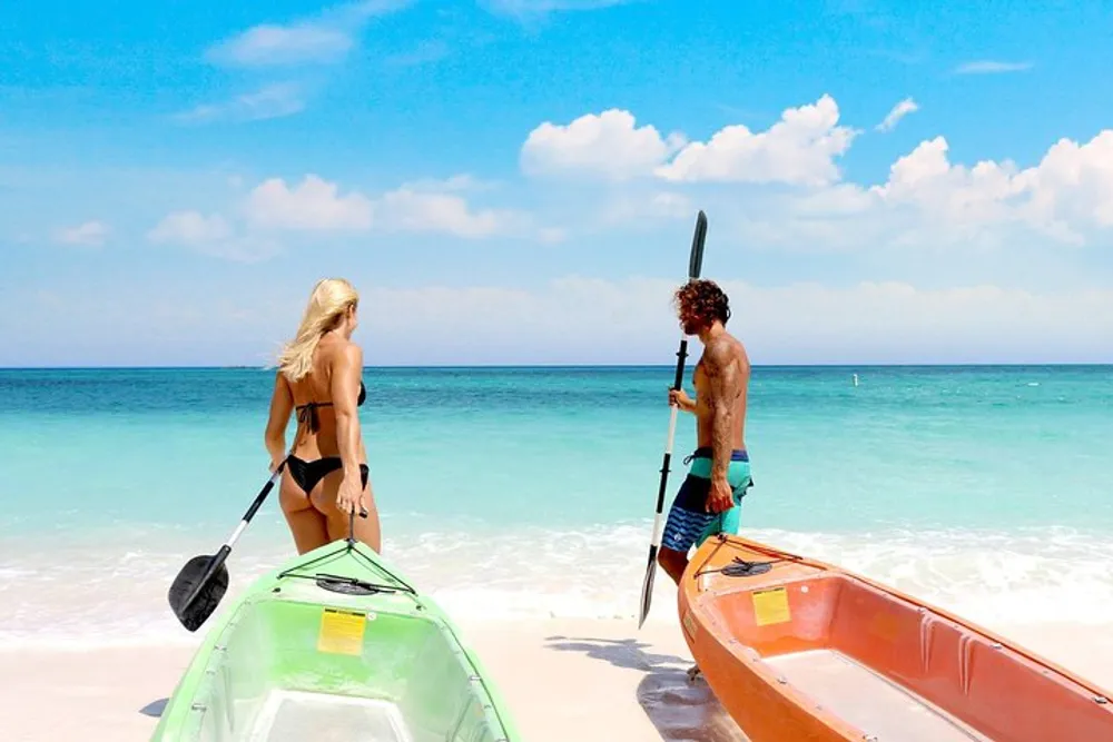 A man and a woman are preparing colorful kayaks on a sunny beach with clear turquoise waters