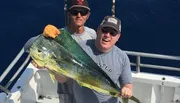 Two men are posing on a boat with a large fish they have caught.