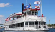 A paddlewheel boat named Carrie B, adorned with flags, sails under a blue sky.