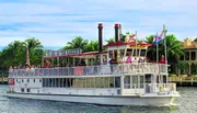 The image depicts a group of passengers enjoying a sightseeing tour on a paddlewheel boat named 