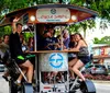 A group of happy people are enjoying a ride on a multi-passenger pedal-powered vehicle in an urban setting