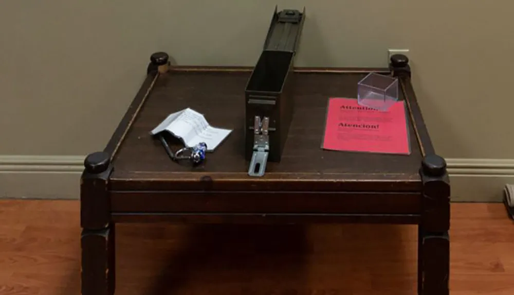 This image shows a wooden table with a few items on it including a metal device a clear cube some papers a keychain and a pink flyer with the word ATTENTION visible on it