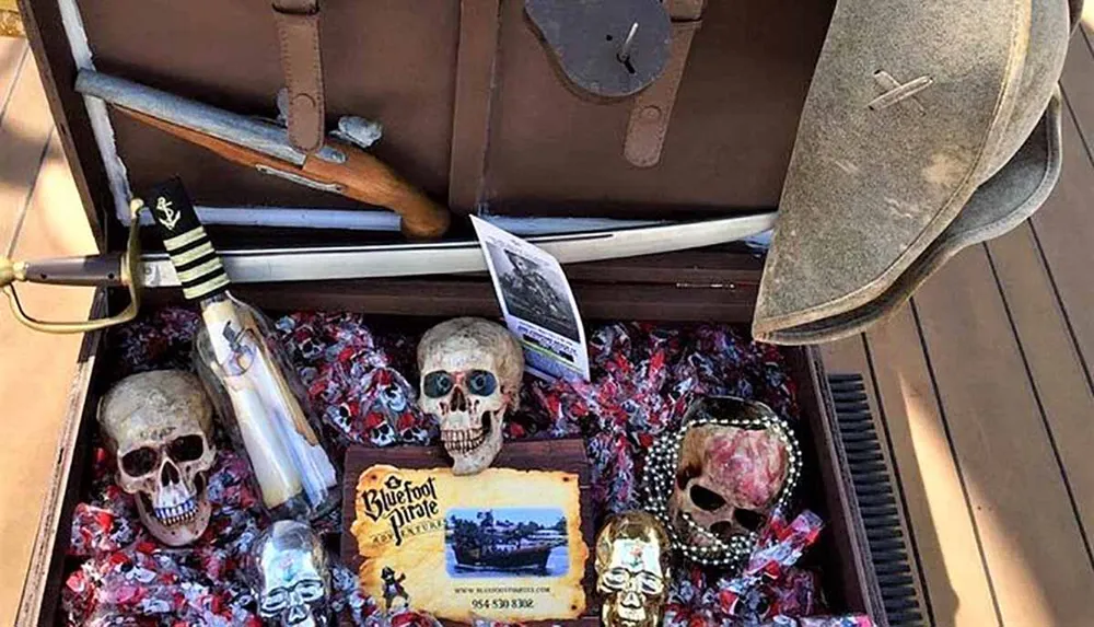 The image features a pirate-themed display with skulls a cutlass a bottle a hat and a flyer indicating it might be for an adventure or attraction presented in an open chest surrounded by what appears to be candy