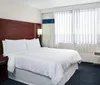 This is a neatly arranged hotel room with a large bed a side table a phone wall-mounted lights a chair and draped windows