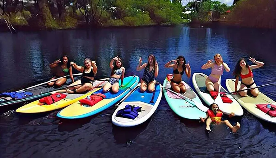 A group of people are enjoying a sunny day paddleboarding on calm water, with some posing for a playful photo.