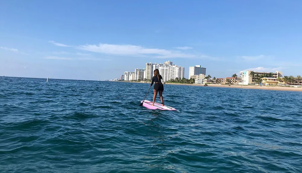A person is paddleboarding on a calm sea with a view of a coastal city skyline in the background