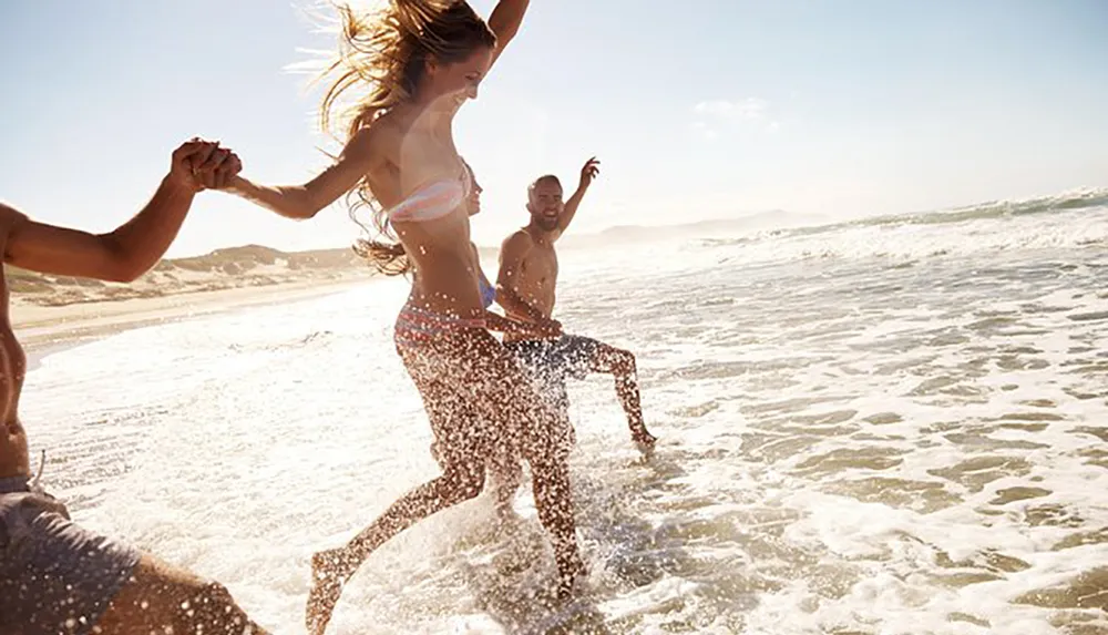 Three joyful people are holding hands and splashing through the surf on a sunny beach