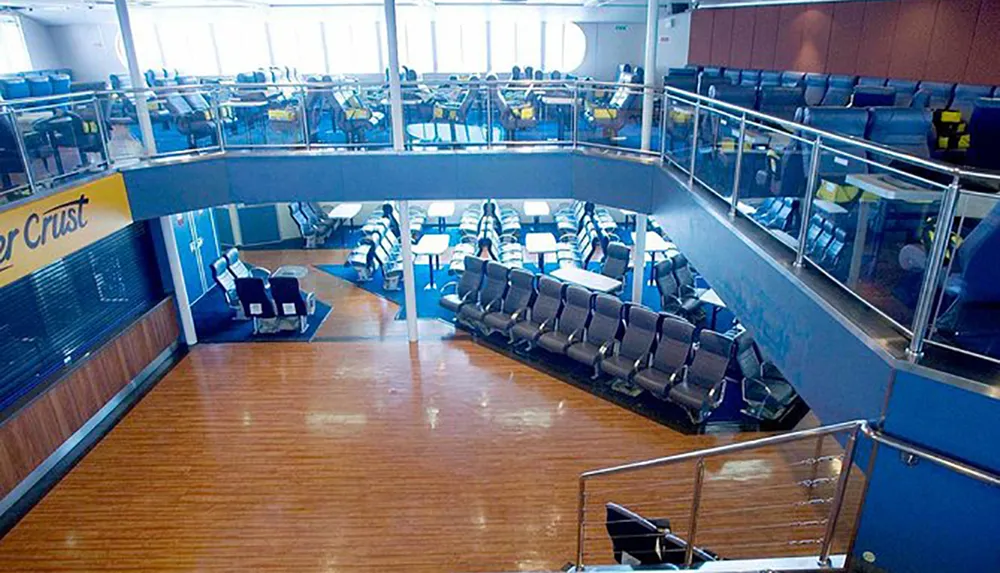 The image shows an empty ferry or ship interior with rows of seating and a closed snack bar showcasing a modern and spacious design with two levels