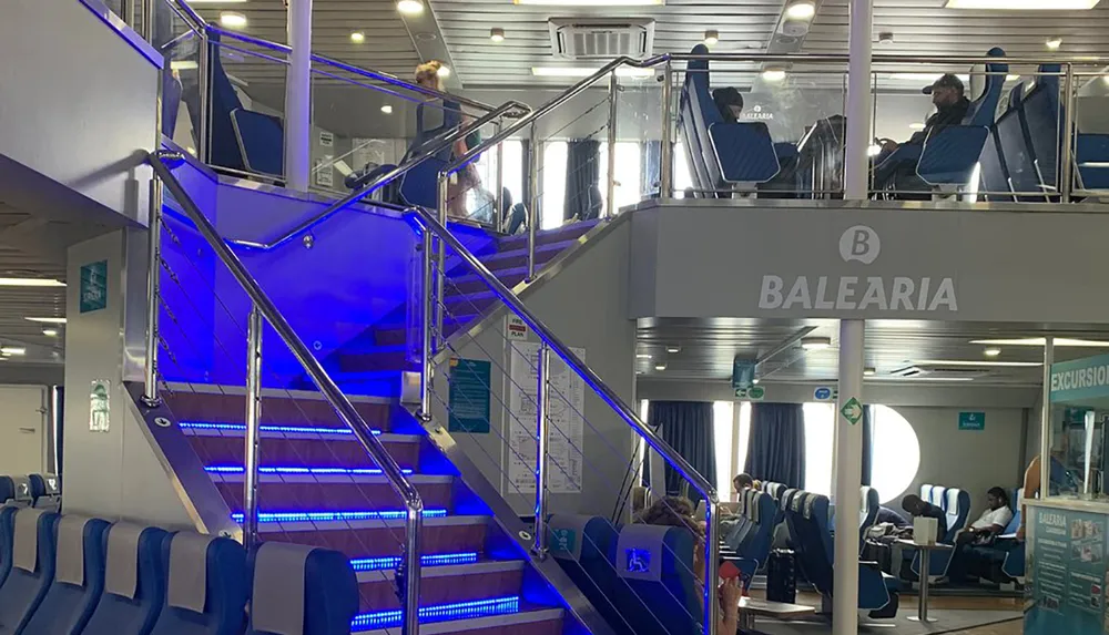 The image shows the interior of a Balearia ferry with passengers seated and walking around featuring a stairway with blue illuminated steps