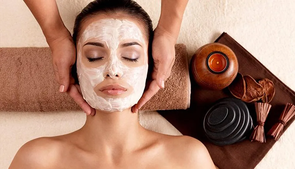 A person is relaxing with a facial mask on while receiving a head massage in a serene spa setting