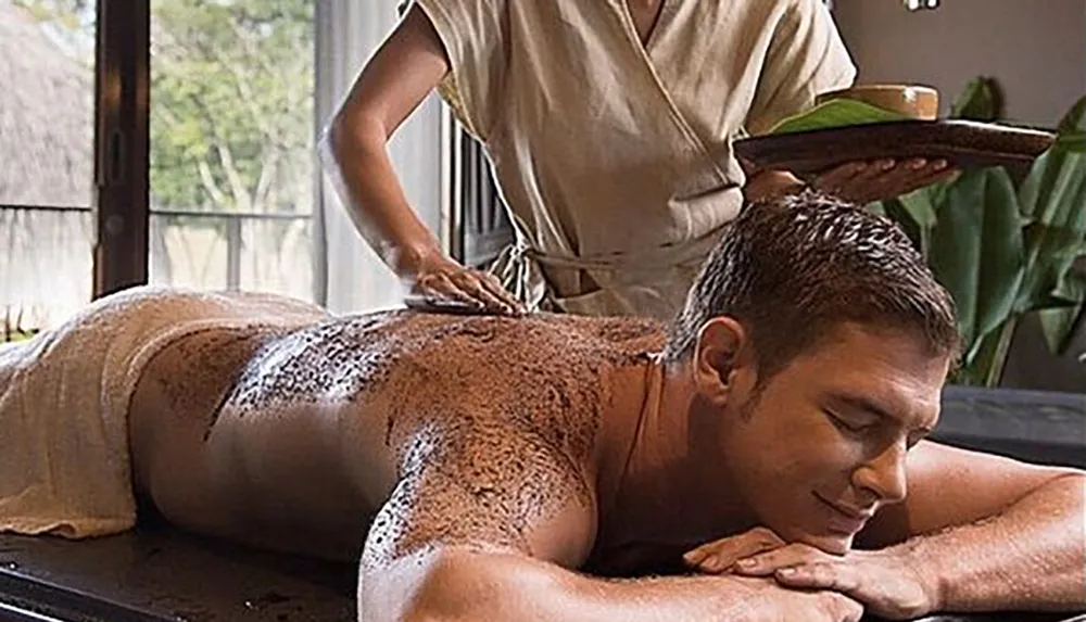 A person is receiving a spa treatment involving a body scrub or mask from a spa therapist in a peaceful setting