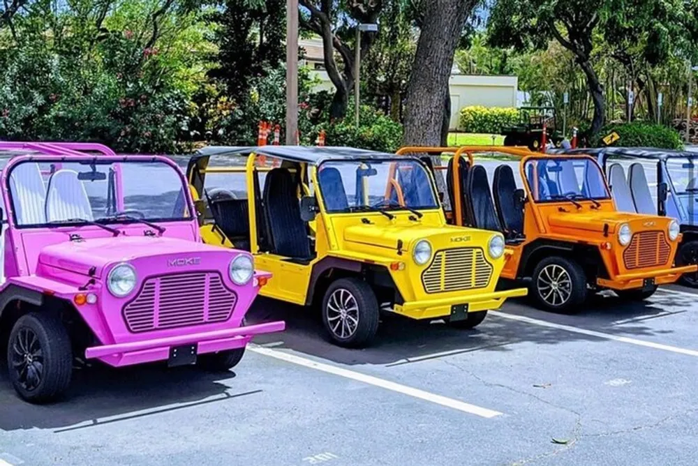 A lineup of brightly colored mini Moke cars parked under the shade of trees