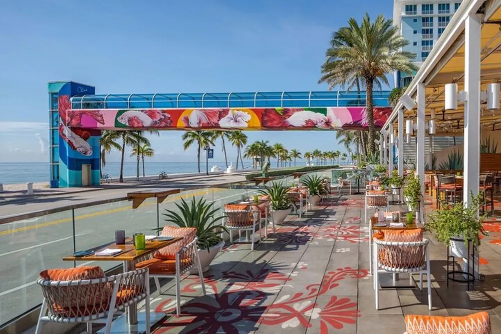 An outdoor dining area with patterned flooring and a tropical view featuring a skybridge with vibrant floral art overhead