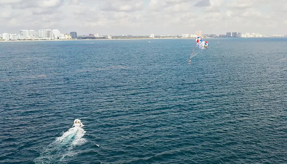 A person is parasailing over the ocean with a city skyline in the background