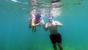 Two people are snorkeling underwater in clear blue water.