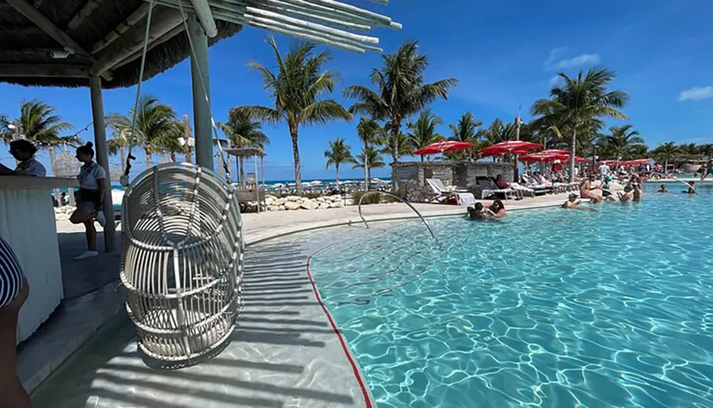 A tropical resort setting with a swimming pool palm trees and people relaxing under the sun with a swing chair in the foreground and a view of the ocean in the background