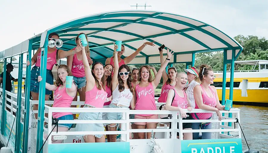 A group of people wearing matching pink tank tops that say bride and bride tribe are enjoying a celebration on a boat.