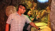 A man and a woman appear to be enjoying an interactive exhibit with rock-like textures and tribal artifacts in the background.