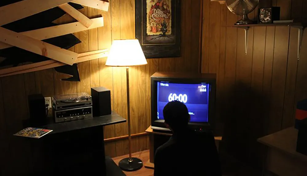 A person sits in front of a television displaying a timer set to 6000 in a cozy wood-paneled room with vintage decor
