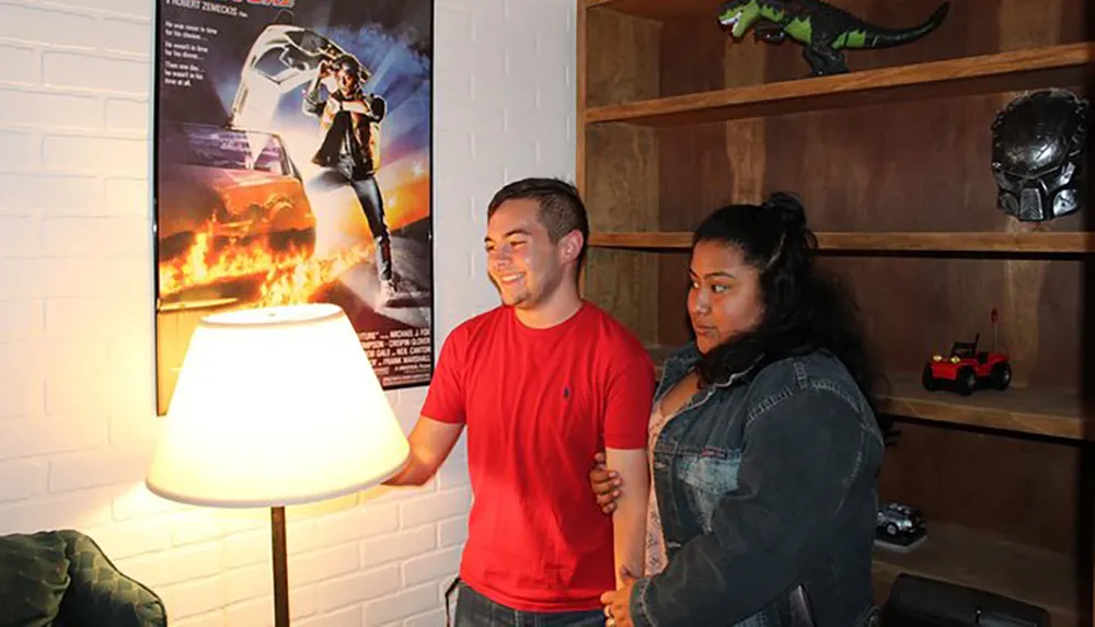 Two people are smiling and standing next to each other in a room adorned with pop culture memorabilia and a movie poster