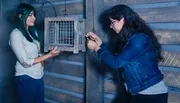 Two women are solving a puzzle involving a cage or box in what appears to be an escape room or interactive game setting.