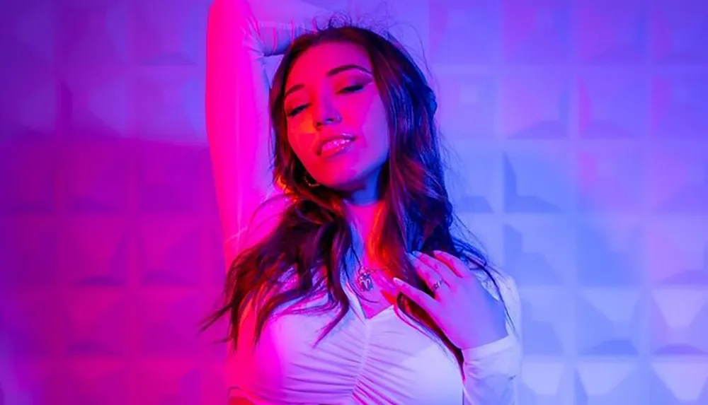 A woman poses with a relaxed expression in a room illuminated by purple and blue lights creating a vibrant atmosphere