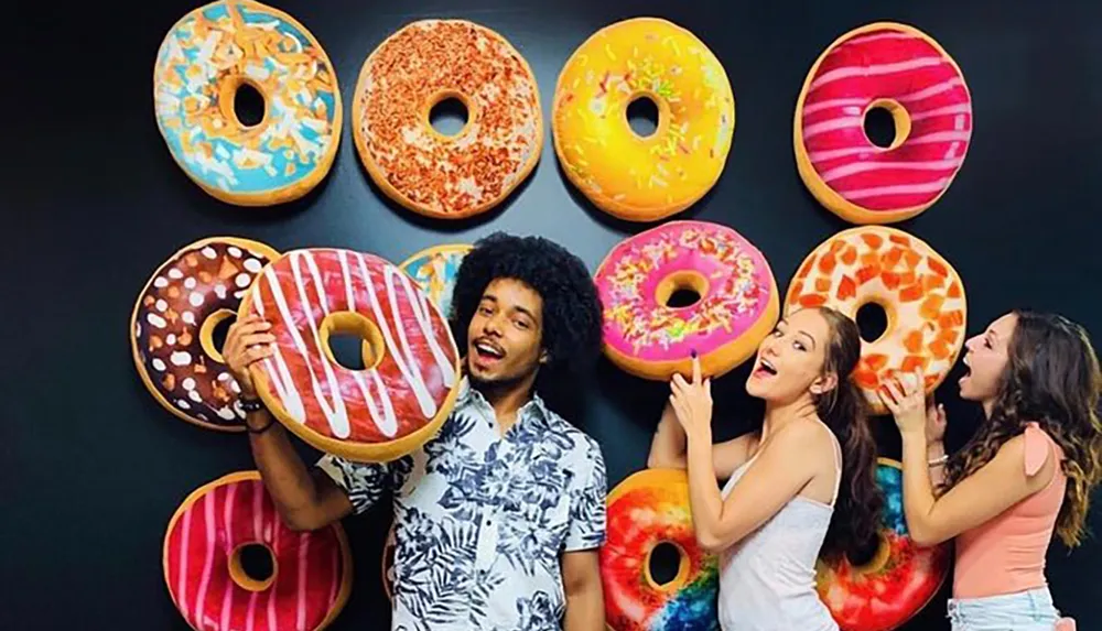 Three people are playfully interacting with large decorative doughnut designs on a wall