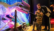 An adult and two children are looking at a brightly illuminated dinosaur exhibit.