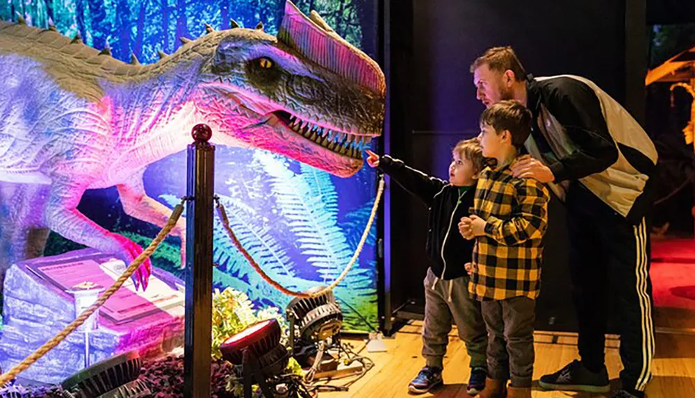 An adult and two children are looking at a brightly illuminated dinosaur exhibit