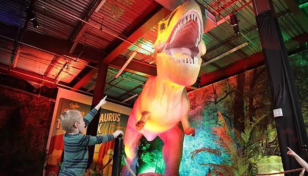 A child is reaching out to a large colorful model of a dinosaur in a display that seems to be part of a museum or exhibit