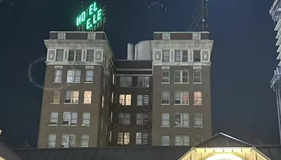 A nighttime image of a multi-story building with the neon sign HOTEL lit at the top and windows illuminated in various rooms.