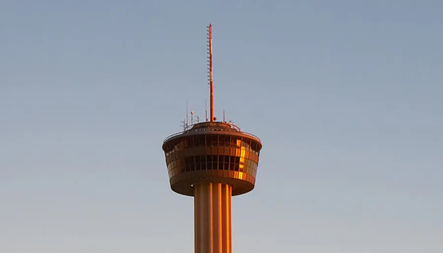 The image captures the upper section of a tall observation tower bathed in warm sunlight against a clear sky.