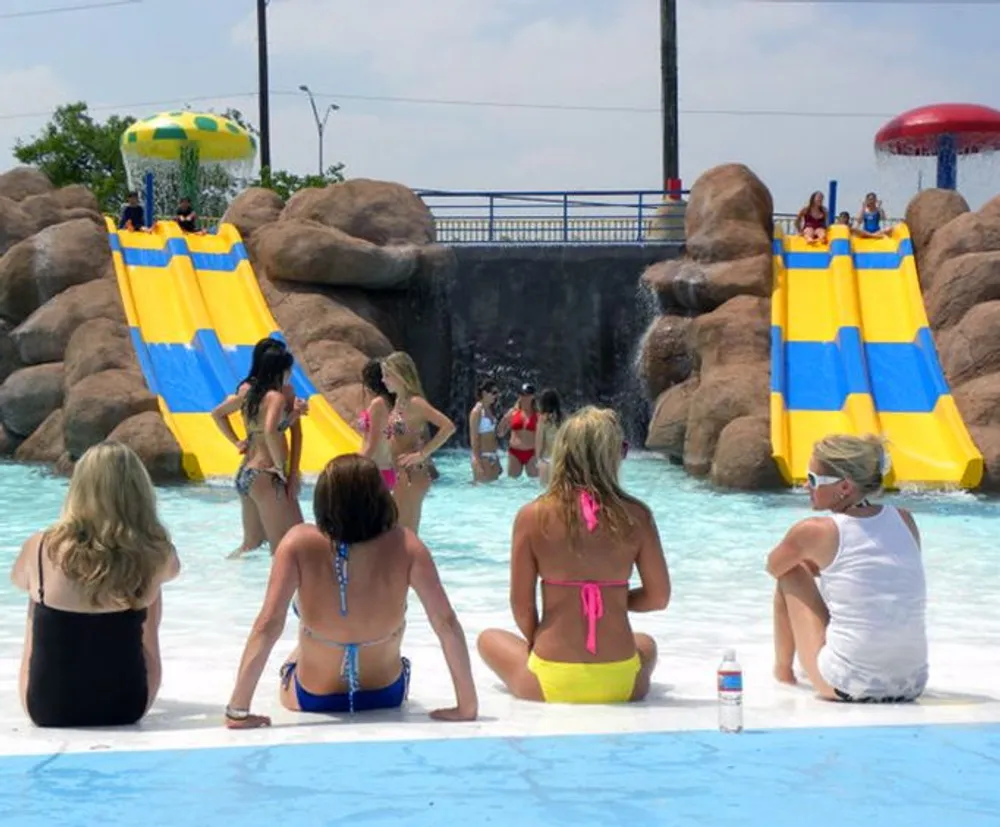 People are enjoying a sunny day at a water park with a waterslide in the background