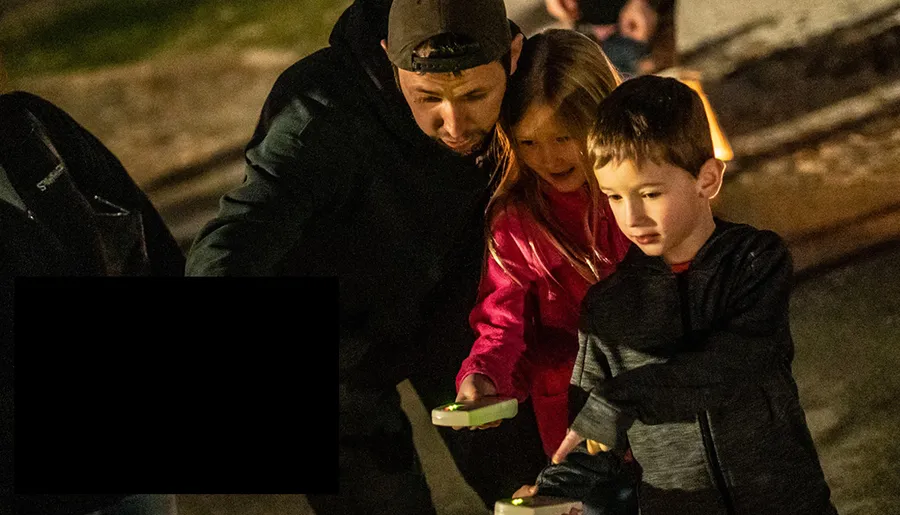 An adult and two children seem engaged in an activity at night while holding what appears to be illuminated objects.
